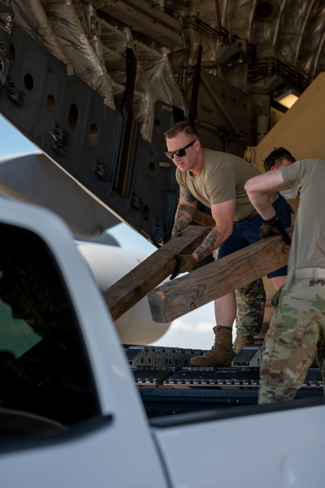 Military member loads wood into the back of a truck.