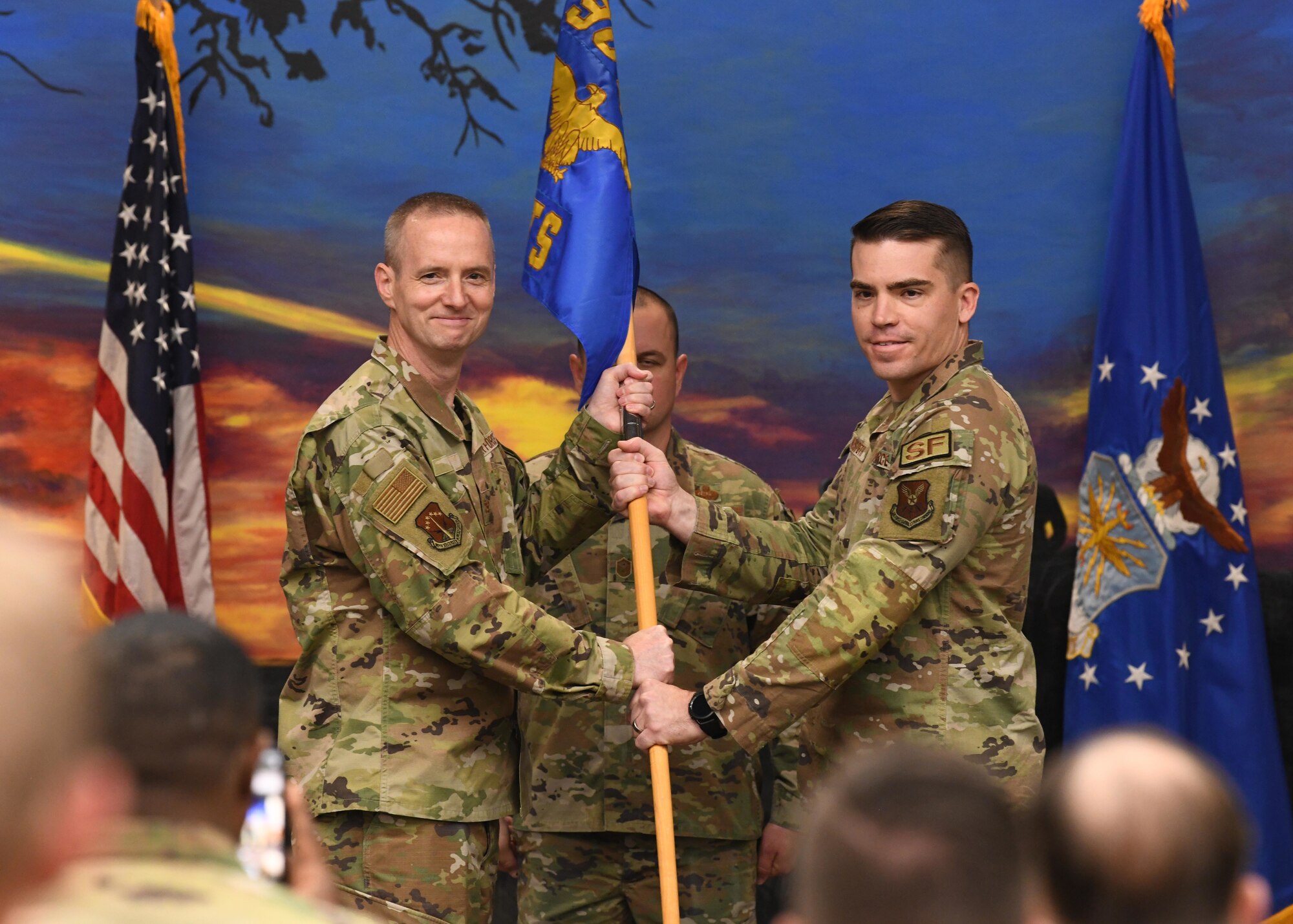 Col. Robert Ford Jr., commander of the 90th Security Forces Group, passes the guidon to Maj. Robert Hudspeth, the incoming commander of the 90th Ground Combat Training Squadron, during a change of command ceremony May 26, 2021 in the Regional Training Institute building at Camp Guernsey, Wyoming. The change of command ceremony signifies the transition of command from Maj. Dexter Binion, the outgoing commander of the 90 GCTS, to Hudspeth. (U.S. Air Force photo by Airman 1st Class Darius Frazier.)