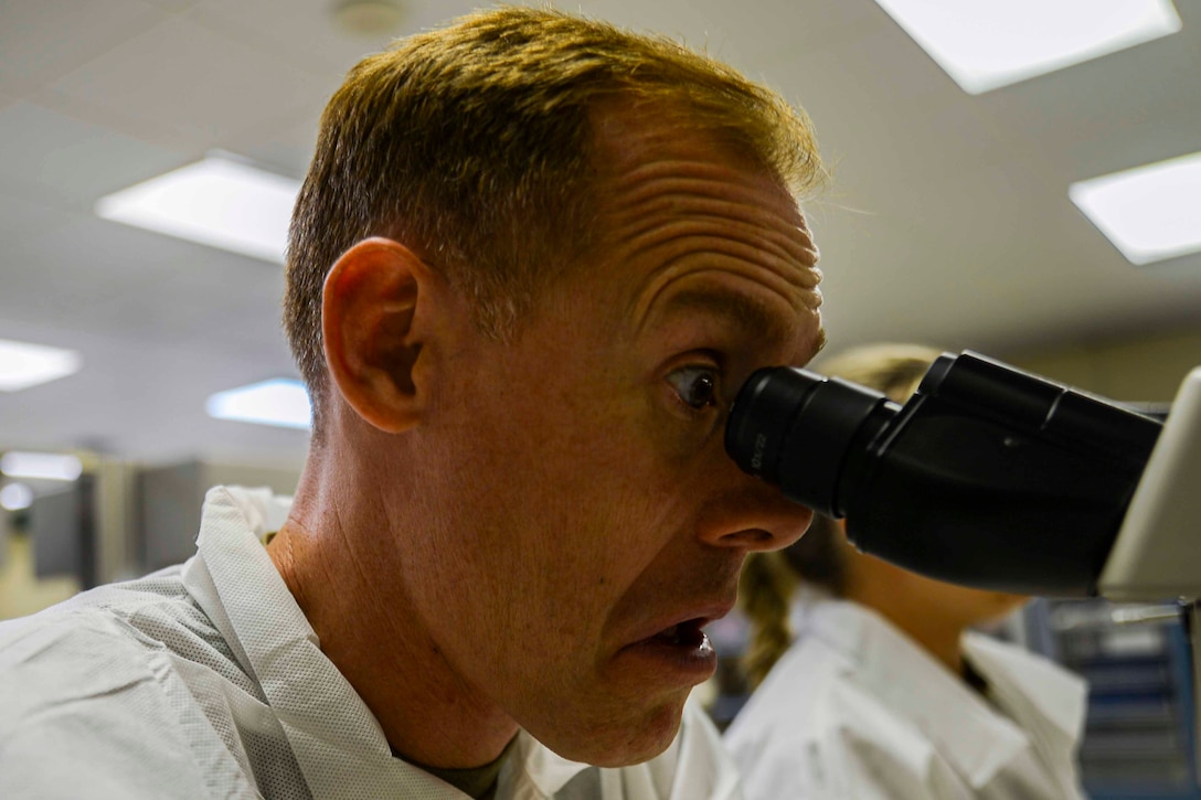 An airman looks into a microscope.