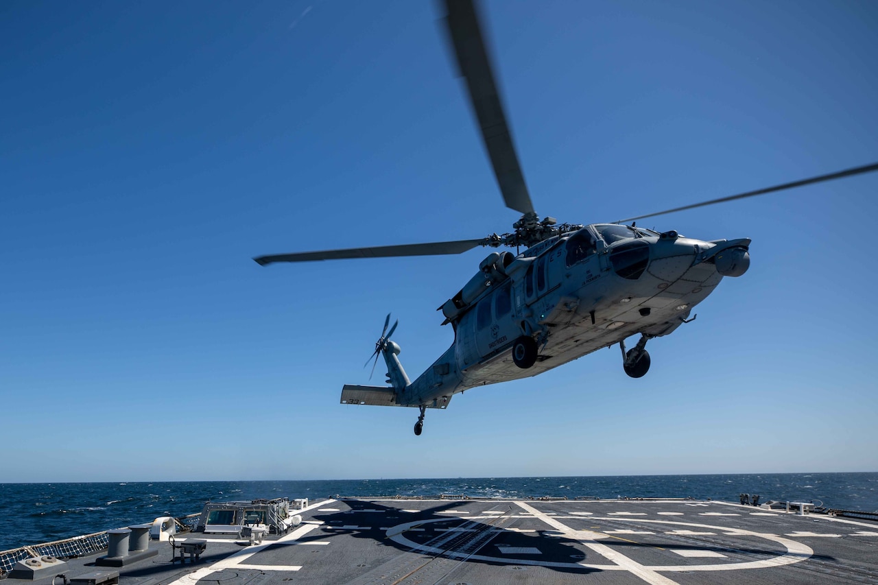 A helicopter hovers above a flight deck.