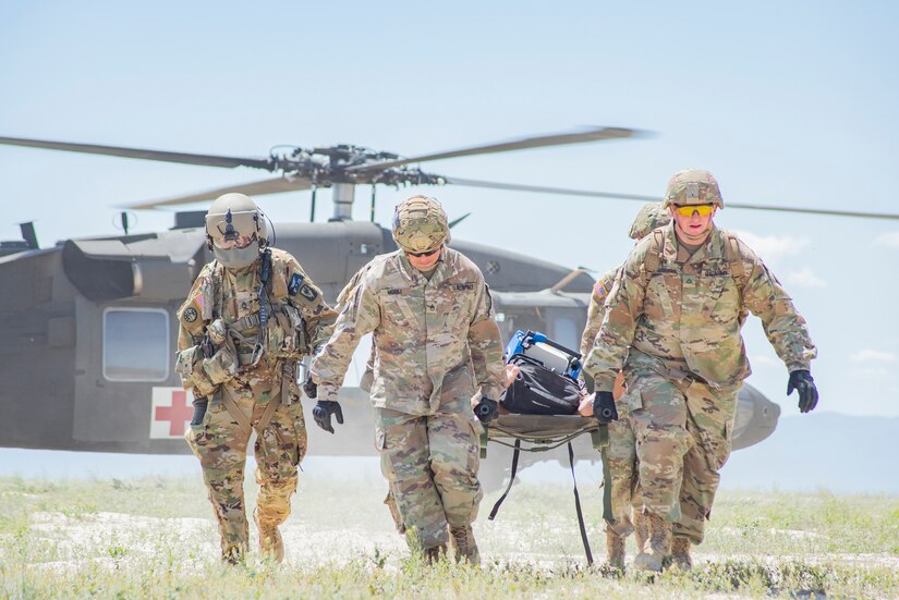 Guardsmen carry a patient on a gurney in front of  a parked helicopter.