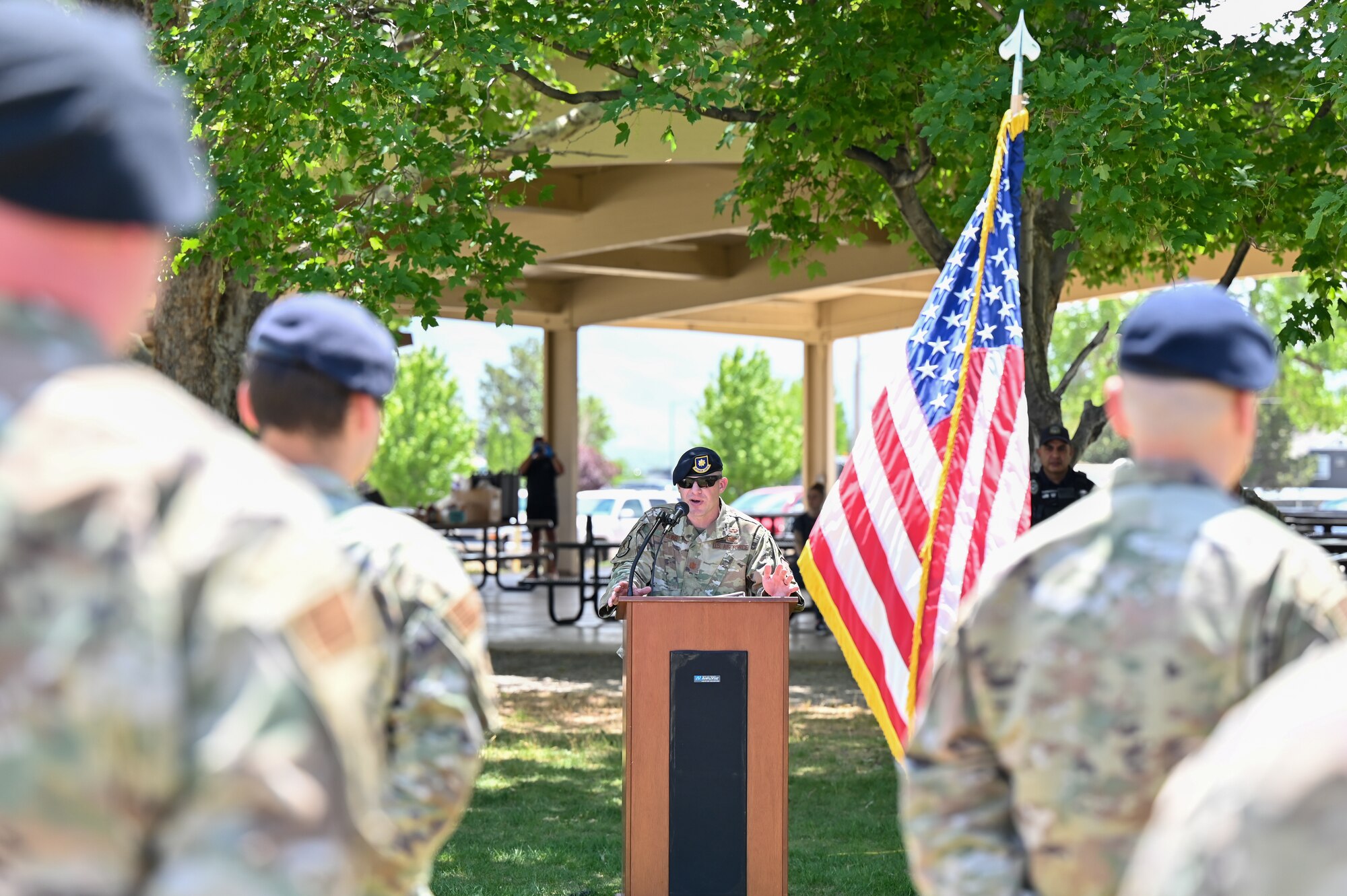 Maj. Doug Dinkins speaks from behind the podium with Airmen in formation in the foreground.