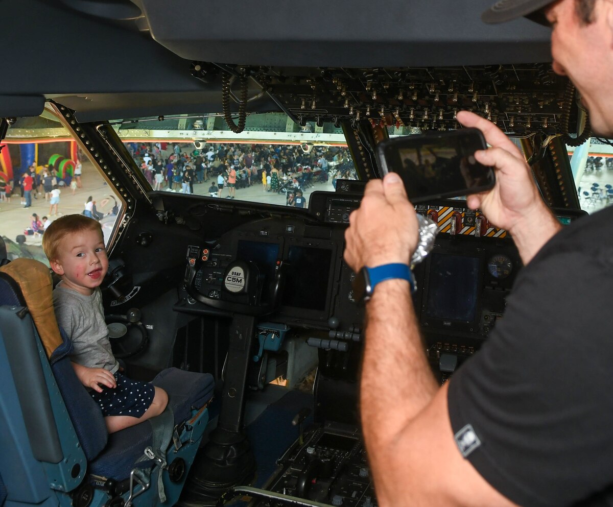 Tech. Sgt. Jeremiah Widder, 433rd Maintenance Squadron aircraft technician, takes a picture of his son sitting in the pilot’s seat inside the C-5M Super Galaxy flight deck at Joint Base San Antonio-Lackland, Texas, May 15, 2022. A static C-5M was one of the attractions as part of the 433rd Airlift Wing Family Day. (U.S. Air Force photo by Airman 1st Class Mark Colmenares)