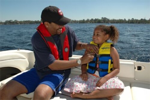 Adult and child in life vests on a boat on the water.