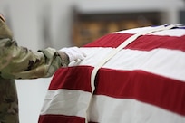 gloved hand makes an adjustment to partially folded flag covering a coffin