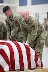 Uniformed soldiers prepare to lift a flag covered coffin