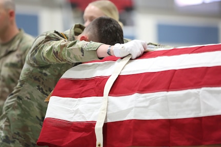Soldier adjusts flag which covers a coffin