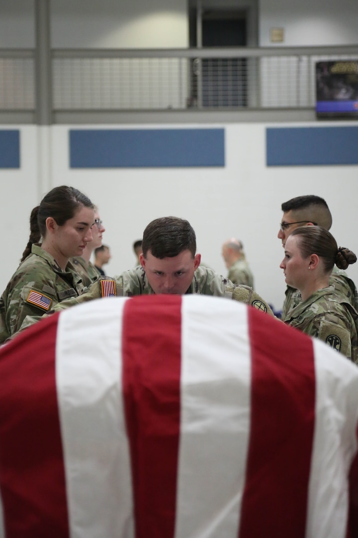 flag covered coffin with uniformed individuals behind it
