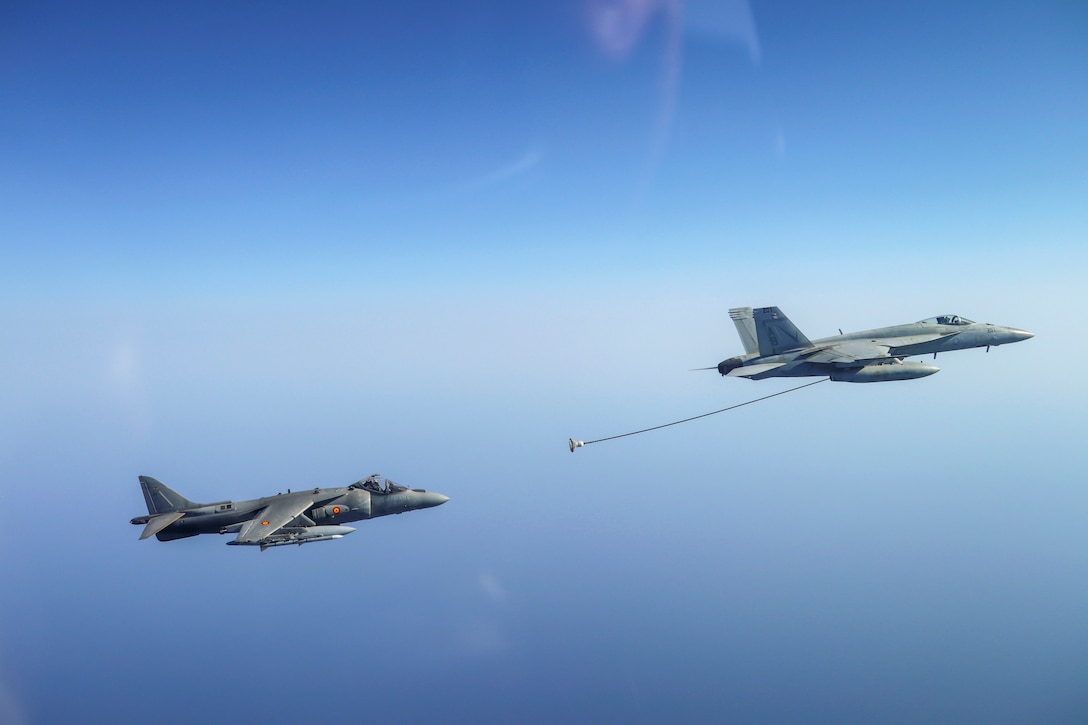 One aircraft extends a line to refuel another aircraft in midair.