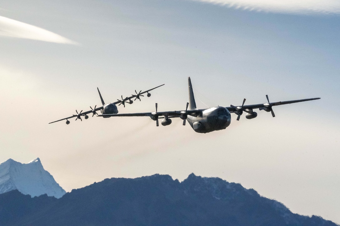 Two aircraft fly near each other with mountains in the background.