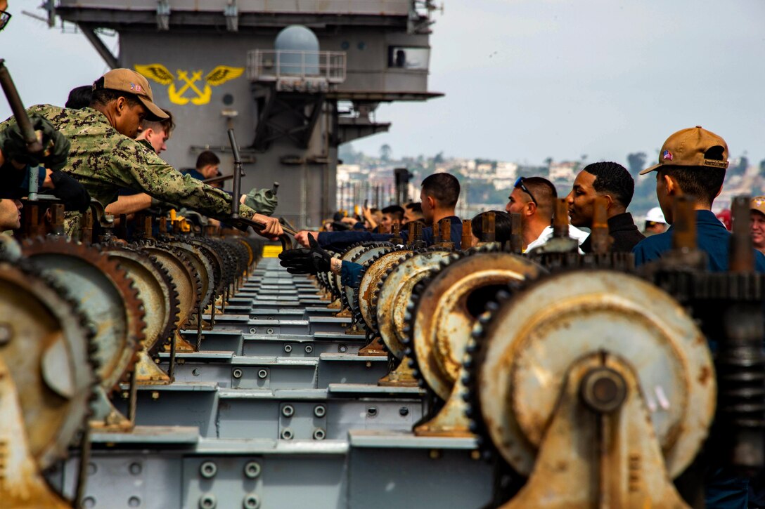 Sailors exchange tools for gears used with aircraft catapults aboard a ship.