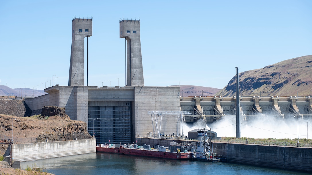 A large vessel travelling along a river prepares to enter a giant concrete basin. The sun is mad shining. Blue skies everywhere. Barren hills sprawl in the distance.