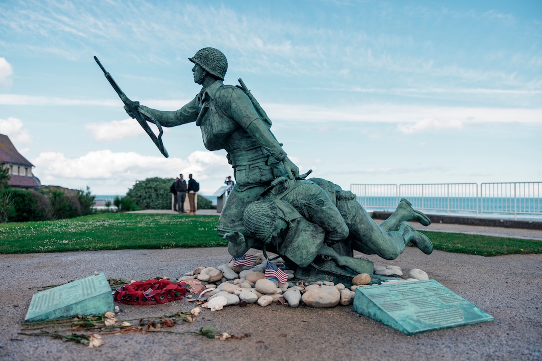 A statue of service members with American flags and flowers in front of it.