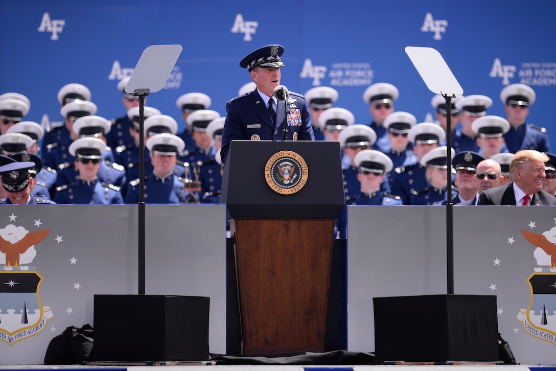 Image of a man speaking on a stage with several people behind him.