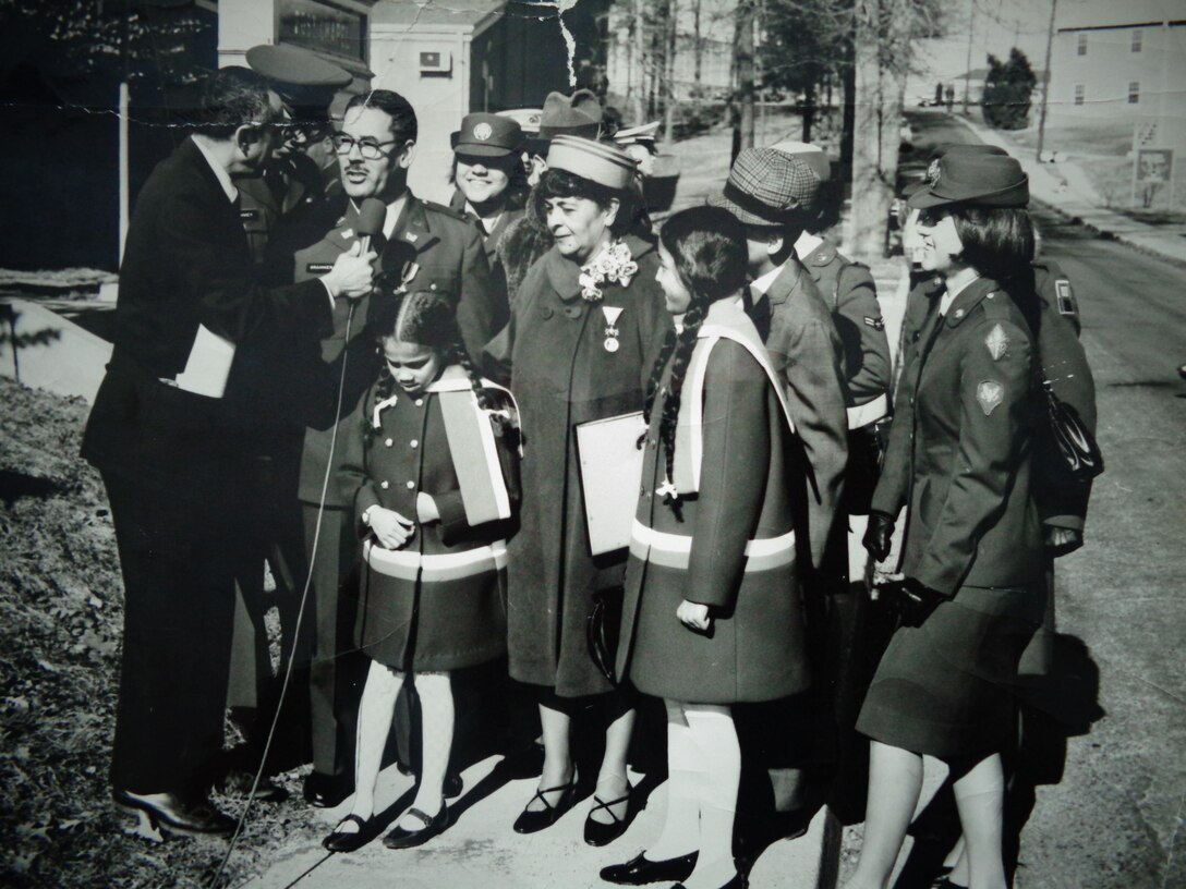 Black and white image of a group of people together, talking to one person on the left.