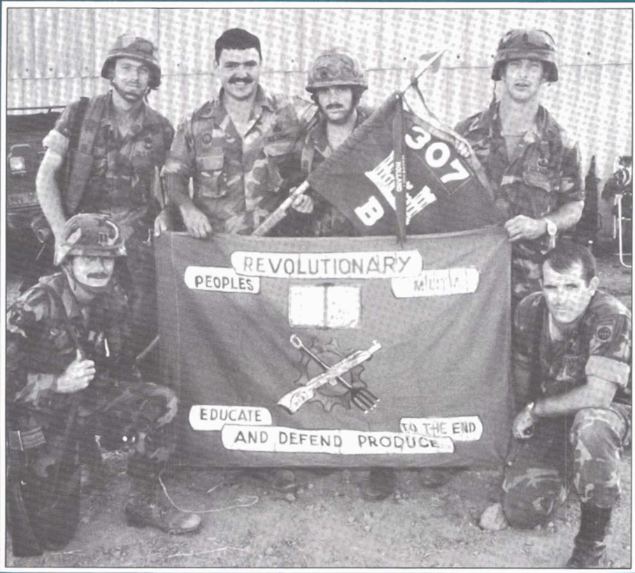 Image of soldiers holding a banner and flag for a picture.