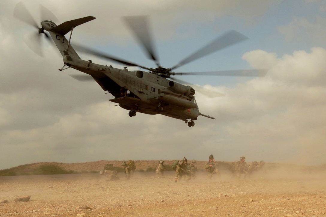 Image of helicoptor in flight with soldiers on the ground below.