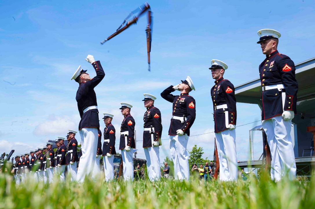 Marines stand in a row as another Marine throws a rifle in the air.