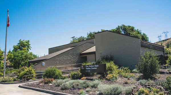 A tan-colored building on a perfectly clear and sunny day, with a sign out front that says "The Dalles Dam Visitor Center."