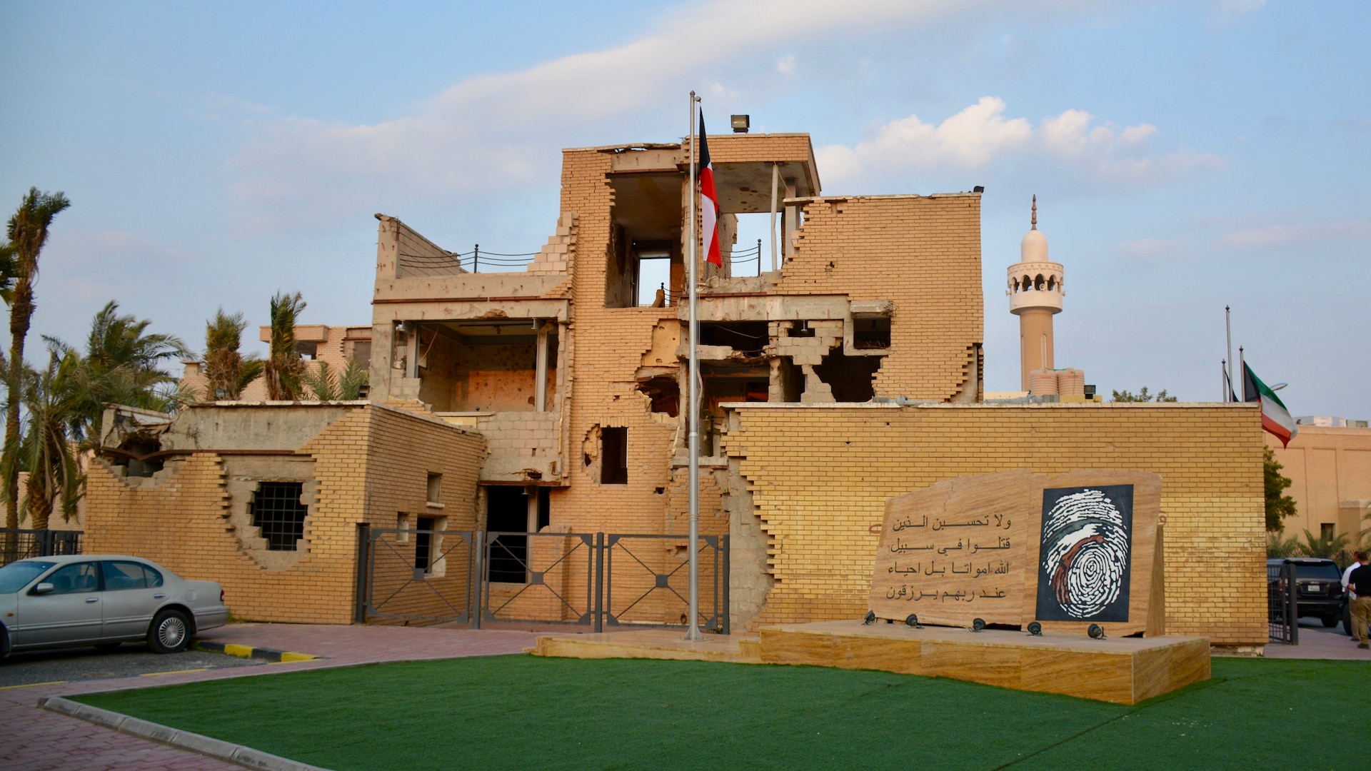 Image of a broken building with a flag and a car.