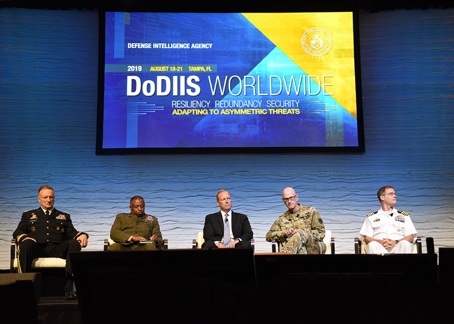 Image of five people sitting, on a stage for the DoDIIS Worldwide Conference.
