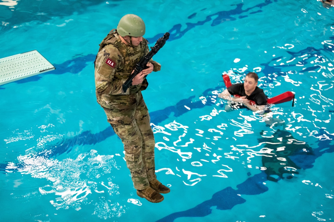 A soldier holding a weapon jumps into a swimming pool.