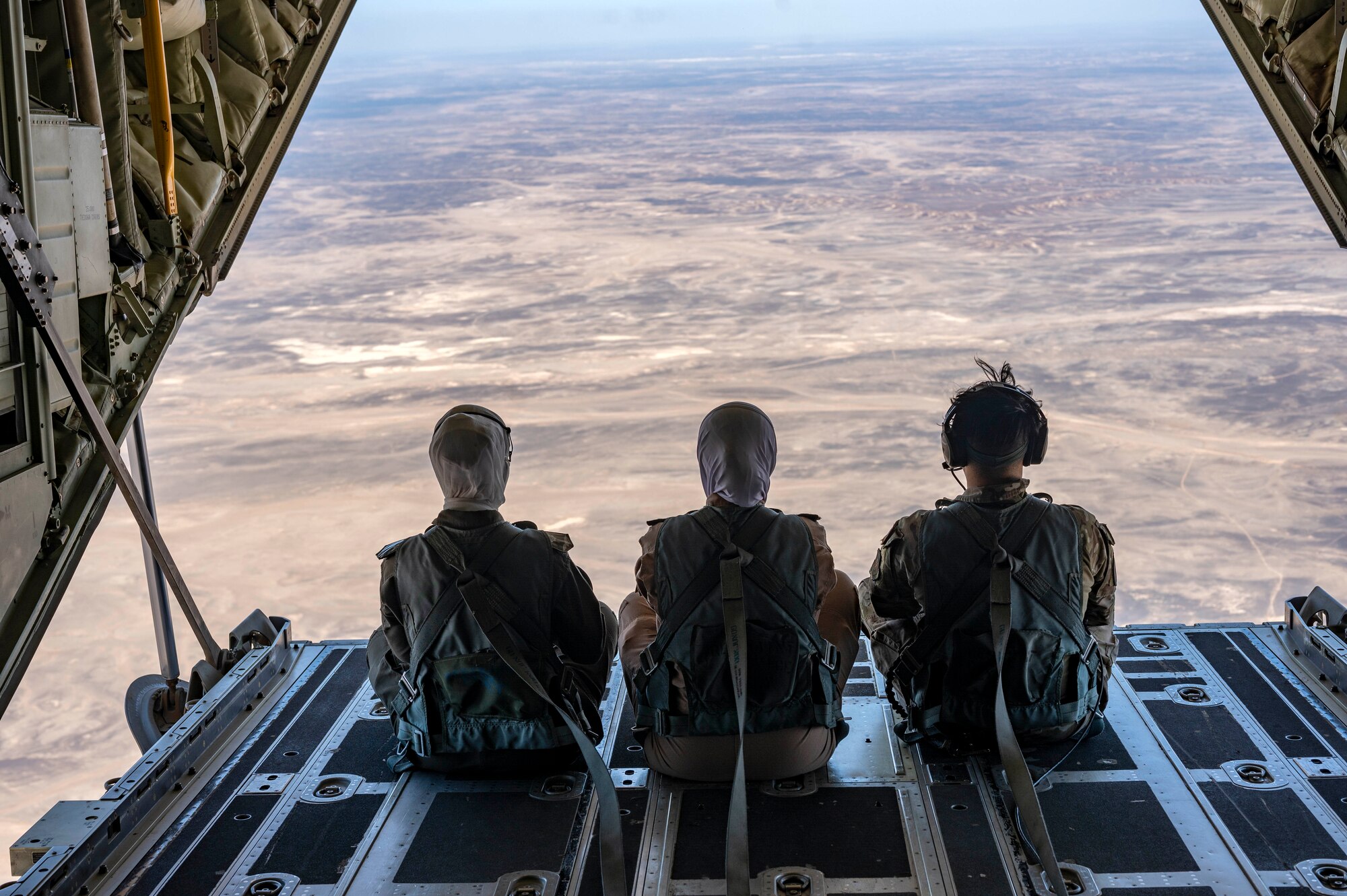 Two Royal Jordanian Air Force female pilots and a U.S. Air Force loadmaster look out from back of an HC-130J Combat King II aircraft during a low-level mission over outlying areas of Wadi Rum, Jordan on May 16, 2022, . The engagement is part of an ongoing partnership between the two countries focused on empowering women in aviation as a way to cultivate and strengthen relationships. (U.S. Air Force photo by Master Sgt. Kelly Goonan)