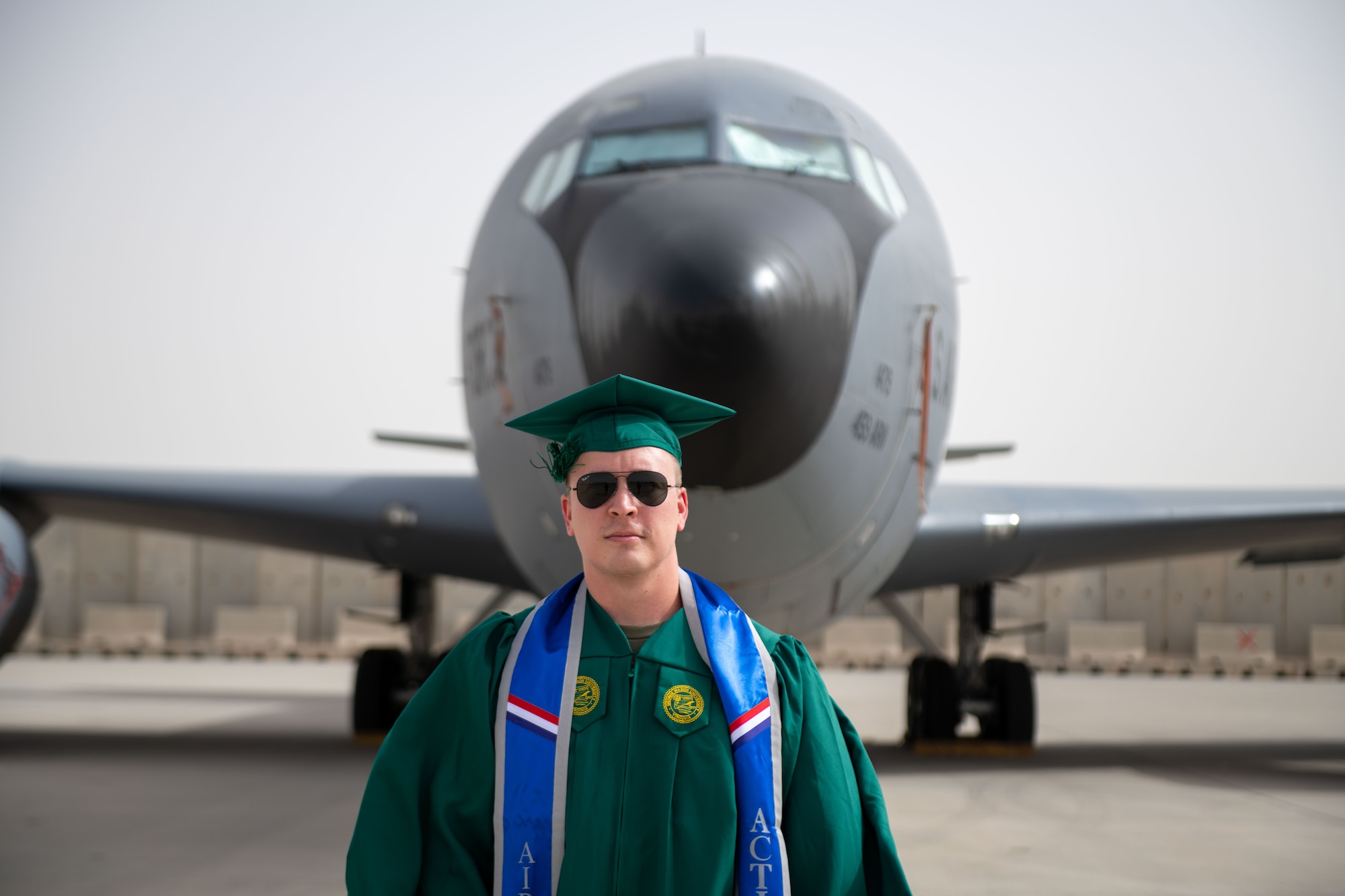U.S. Air Force Staff Sgt. Nicholas Kremposky poses in front of a KC-135 while wearing a graduation cap and gown on Al Udeid Air Base, Qatar, May 26, 2022. Kremposky completed his bachelors degree, and is currently pursuing a masters degree with a goal of becoming a pilot. (U.S. Air National Guard photo by Airman 1st Class Constantine Bambakidis)