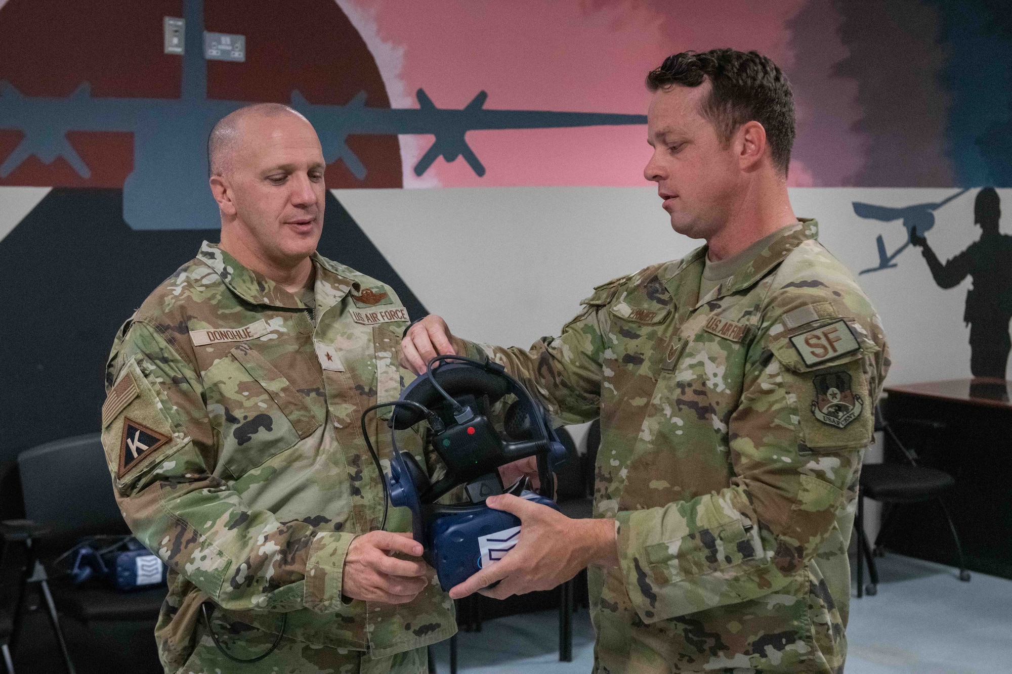 U.S. Air Force Tech Sgt. Jesse Ermer, a 379th Air Expeditionary Security Forces Squadron member, demonstrates to U.S. Air Force Brig. Gen. Gerald Donohue, 379th Air Expeditionary Wing Commander, how to use a virtual reality headset on Al Udeid Air Base, Qatar, May 24, 2022. The headset is part of a new training tool that security forces received, called the Street Smart VR Simulator. (U.S. Air National Guard photo by Airman 1st Class Constantine Bambakidis)