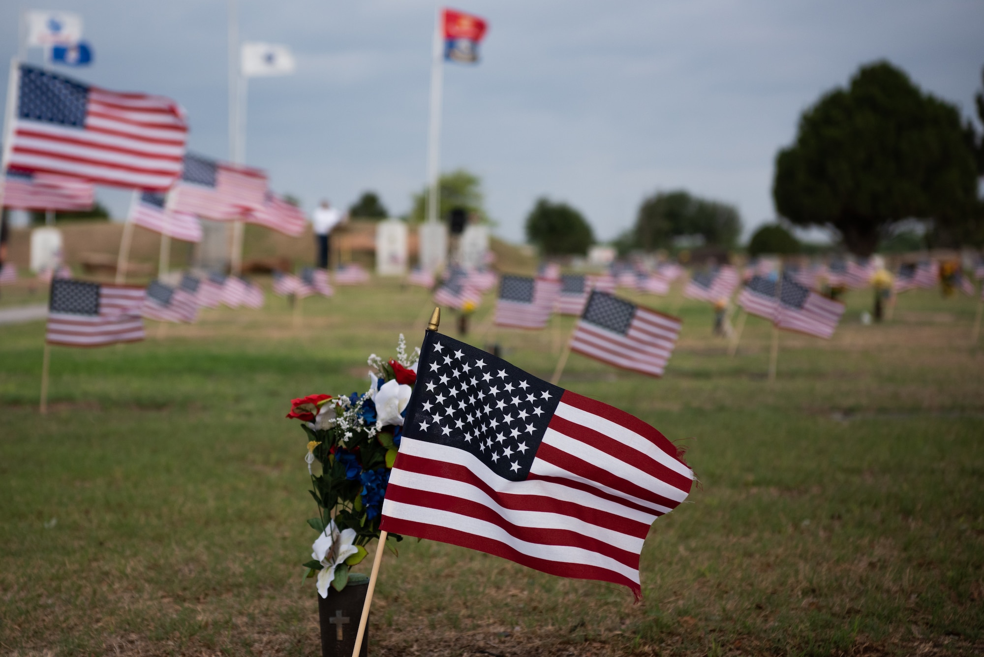 The American flag ruffles in the breeze alongside a vase of flowers atop a headstone at Lawnhaven Memorial Gardens, San Angelo, Texas, May 30, 2022. Flags were planted by volunteers from the San Angelo community and Lawnhaven staff at every service member’s grave in preparation of a Memorial Day ceremony (U.S. Air Force photo by Senior Airman Michael Bowman)