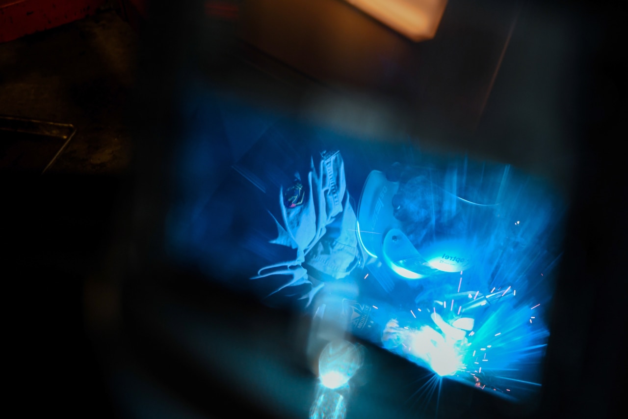 A smoky view of someone welding is illuminated by blue light.