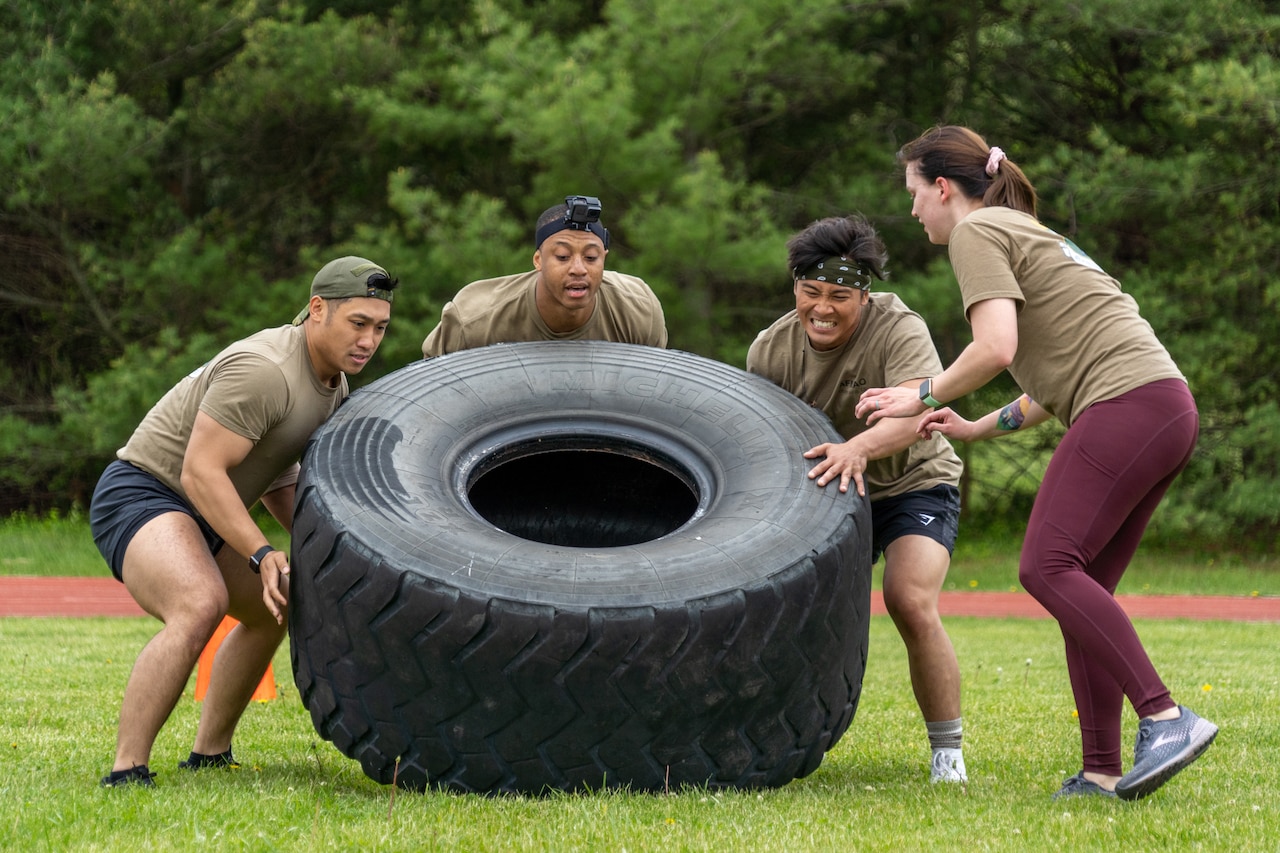 Airmen work to move a large tire in a field.