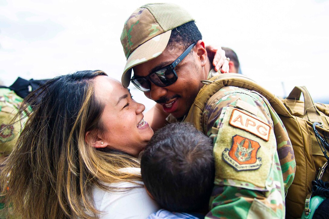 An airman hugs a woman and a child.