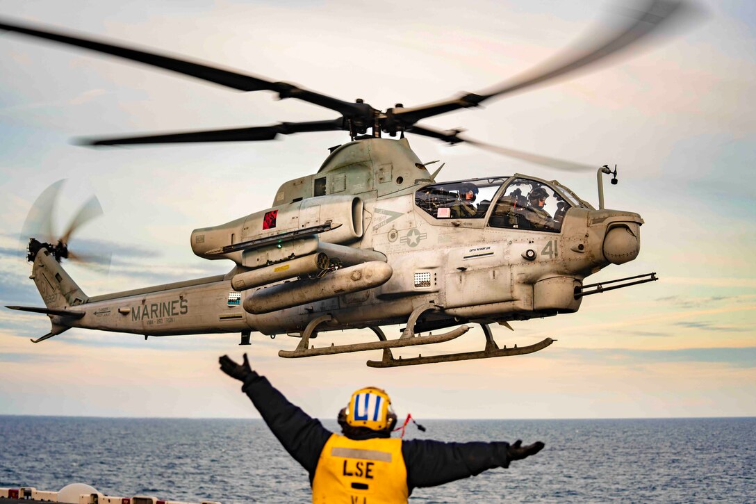 A sailor signals toward an airborne helicopter.
