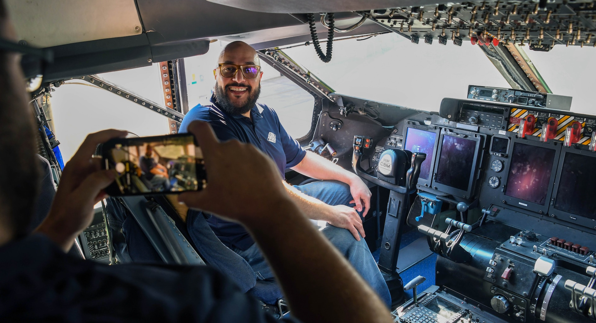 USAA employees take photos while in the cockpit of a 433rd Airlift Wing C-5M Super Galaxy May 17, 2022, at Joint Base San Antonio-Lackland, Texas. The visit from USAA included a briefing on wing capabilities, a tour of the C-5M Super Galaxy aircraft and a virtual reality training demonstration. (U.S. Air Force photo by Kristian Carter)