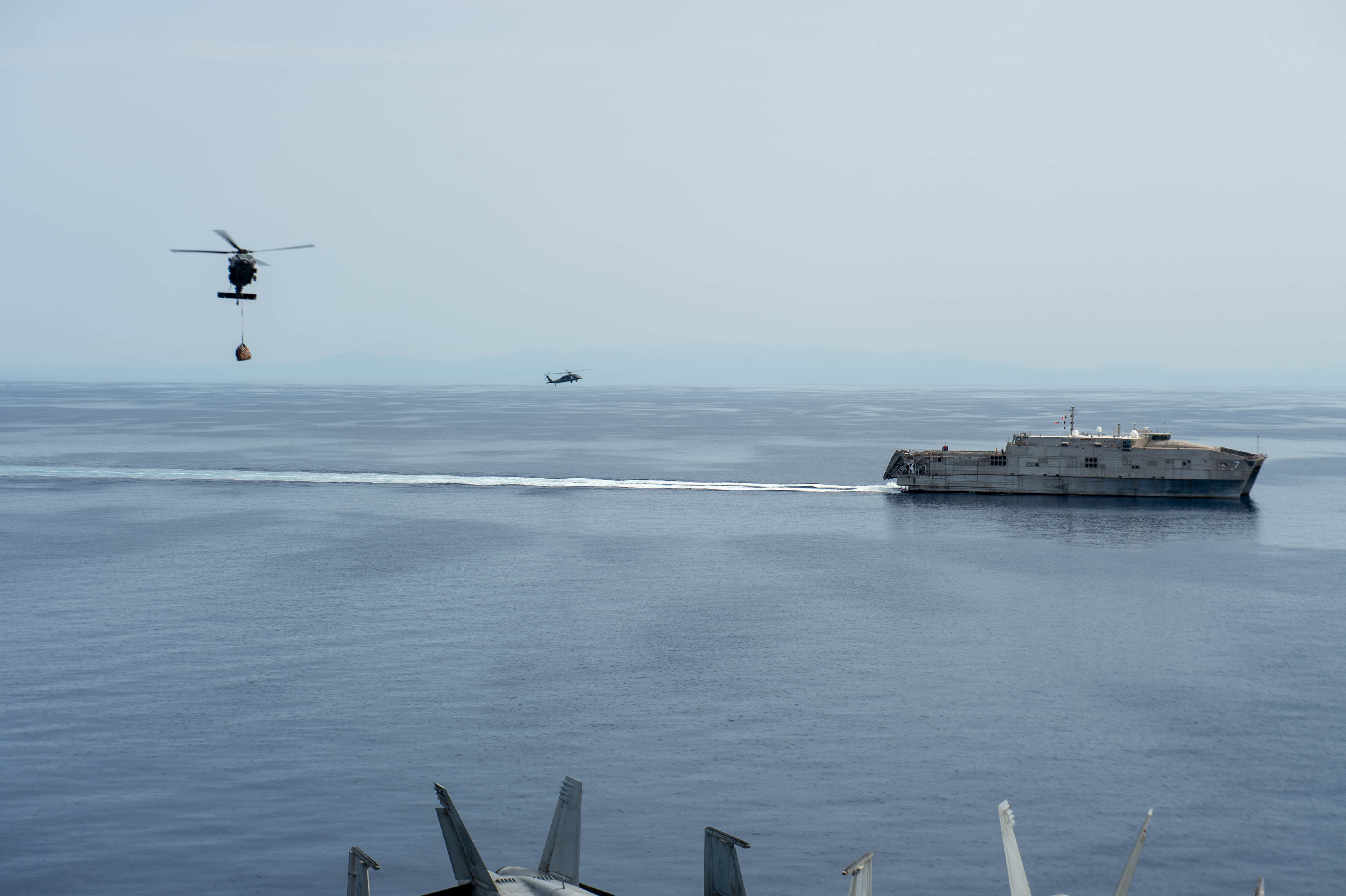 An MH-60S Sea Hawk, attached to the "Dragon Slayers" Helicopter Sea Combat Squadron (HSC) 11, transports stores from the Spearhead-class expeditionary fast transport ship USNS Carson City (T-EPF-7) to the aircraft carrier USS Harry S. Truman (CVN75) during a replenishment-at-sea, May 27, 2022.