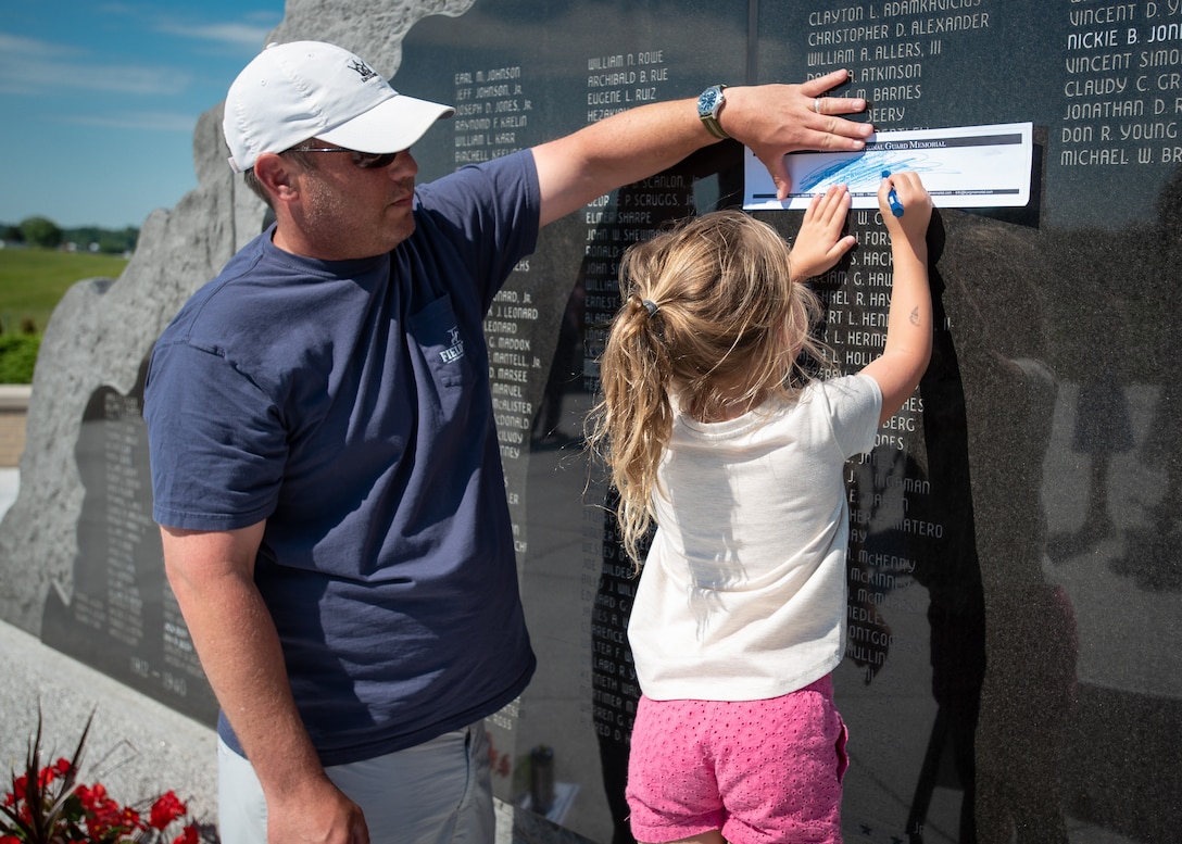 Adam Nielsen, a former Kentucky National Guard Soldier, receives some assistance with a rubbing of the name of a fallen comrade, Staff Sgt. Nicholas R. Carnes, following a memorial service at Boone National Guard Center in Frankfort, Ky., May 30, 2022, honoring members of the Kentucky Guard who died in the line of duty. Carnes, who was killed in a firefight in Afghanistan on Aug. 26, 2007, was Nielsen’s squad leader during the deployment. (U.S. Air National Guard photo by Dale Greer)