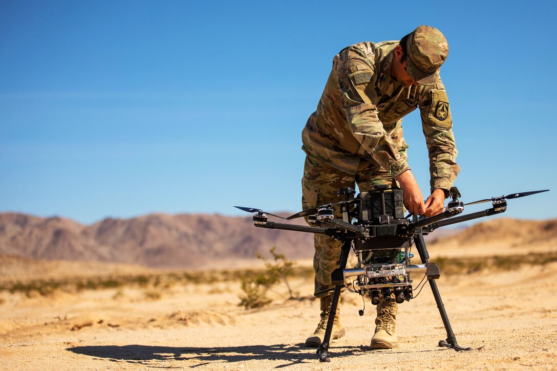 A soldier makes an adjustment to a drone sitting in a field.
