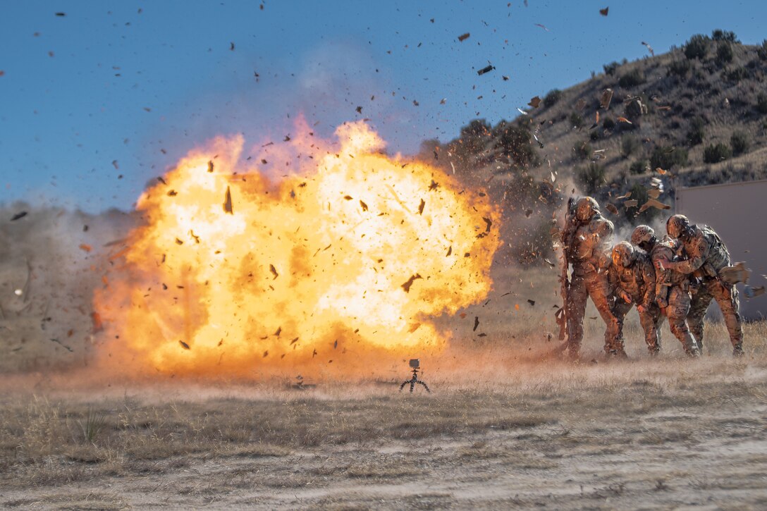 A door explodes sending debris through the air as a group of soldiers line up behind a shield.