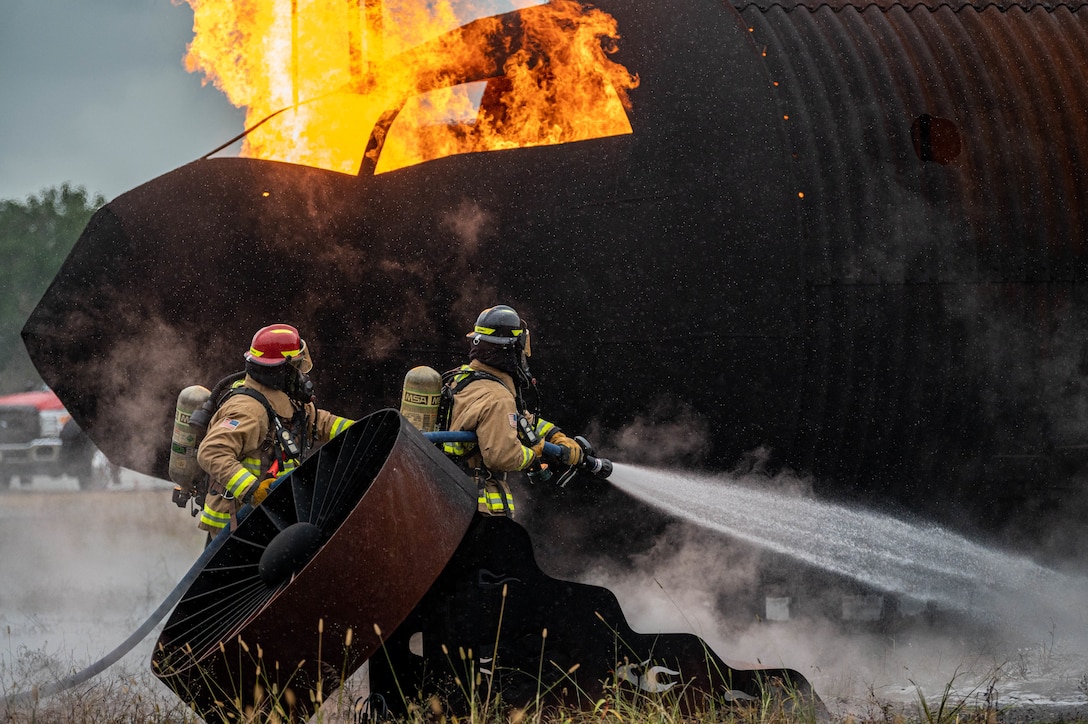 U.S. Air Force Staff Sgt. Seth Warner (left) and Airman 1st Class Kollin Money, both firefighters with the 633d Civil Engineer Squadron, operate the front end of the hose to extinguish the flames on a small aircraft trainer at Joint Base Langley-Eustis, Virginia, Oct. 13, 2022.