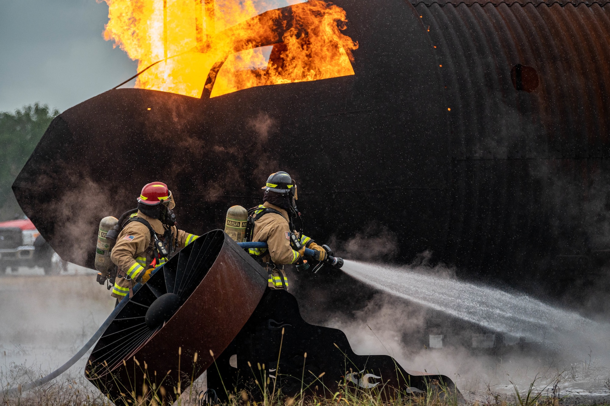 U.S. Air Force Staff Sgt. Seth Warner (left) and Airman 1st Class Kollin Money, both firefighters with the 633d Civil Engineer Squadron, operate the front end of the hose to extinguish the flames on a small aircraft trainer at Joint Base Langley-Eustis, Virginia, Oct. 13, 2022.