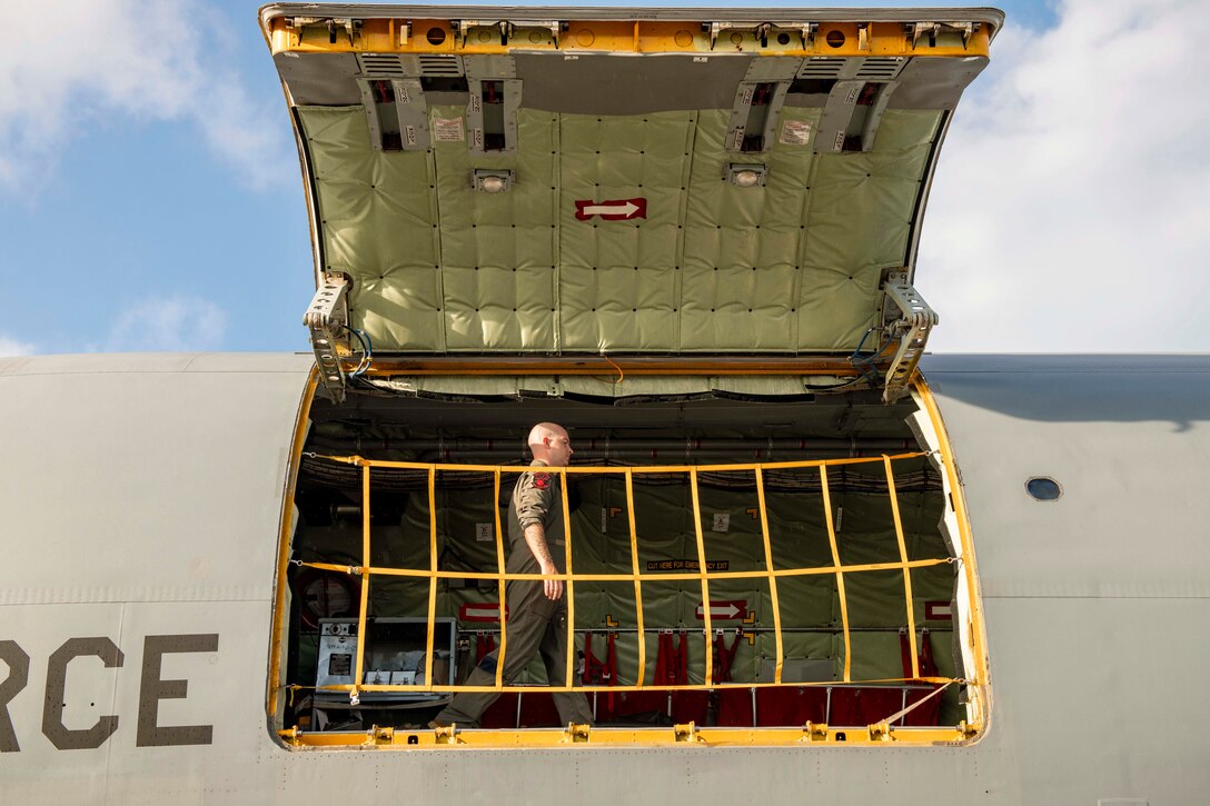 An airman walks across an aircraft as seen from an open door.