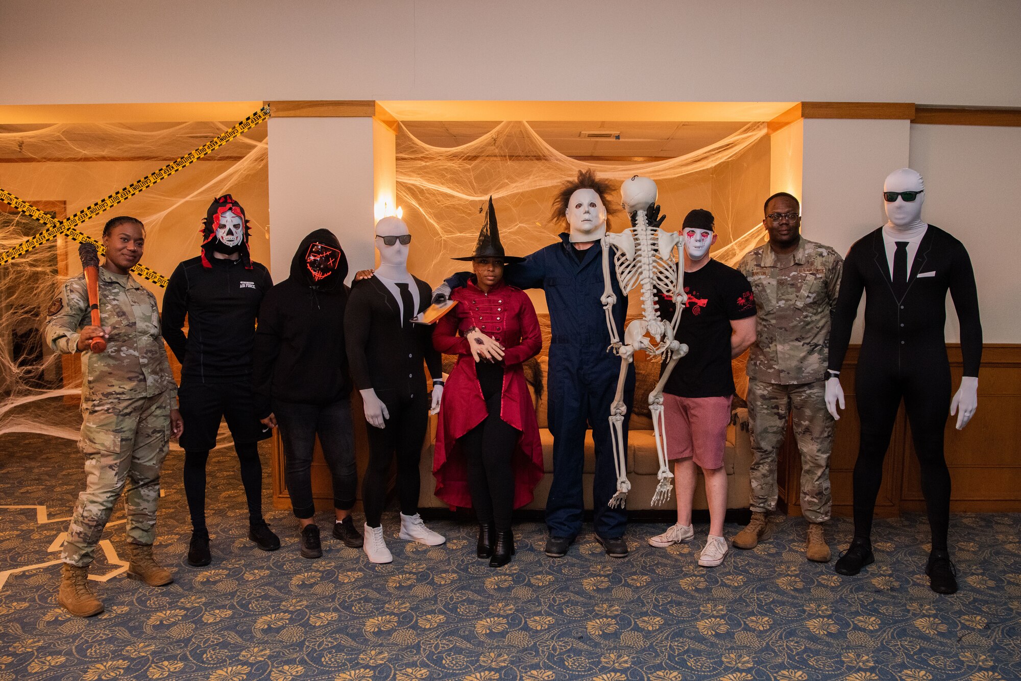 A group of people pose for the camera. The shot is full-length of their body, two people are in an Air Force uniform and the rest are in Halloween costumes.