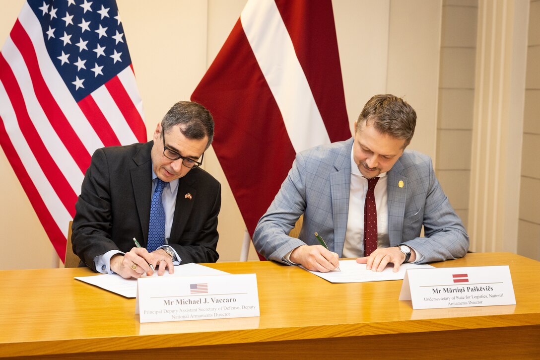 Two men sit at a desk and sign documents