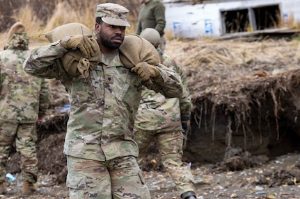 Alaska Army National Guard Spc. Sharhan Sylva, a wheeled vehicle mechanic, 207th Aviation Regiment, carries sandbags to reinforce the Koyuk Native Store warehouse for Operation Merbok Response in Koyuk, Alaska Sept. 28, 2022. More than 130 members of the Alaska Organized Militia, which includes members of the Alaska National Guard, Alaska State Defense Force and Alaska Naval Militia, were activated following a disaster declaration issued Sept. 17 after the remnants of Typhoon Merbok caused dramatic flooding across more than 1,000 miles of Alaskan coastline. (Alaska National Guard photo by Sgt. Seth LaCount)