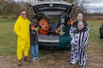 Family dressed in costumes standing by a vehicle decorated for Halloween.