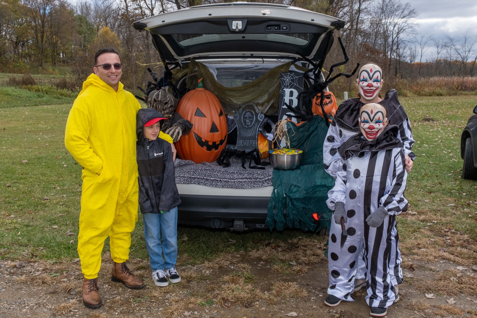 Family dressed in costumes standing by a vehicle decorated for Halloween.