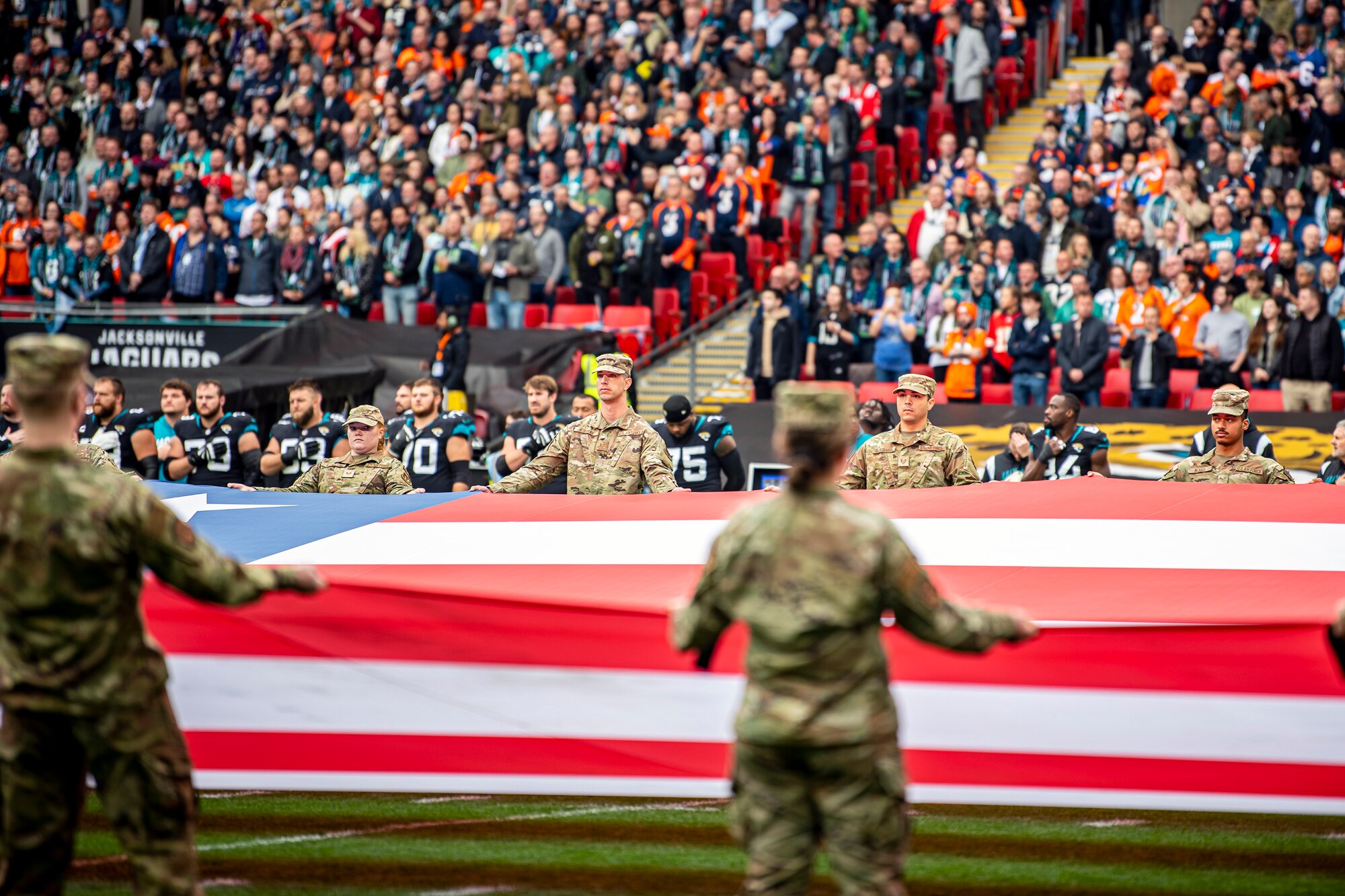 Airmen from the 501st Combat Support Wing unveil an American flag during the national anthem at Wembley Stadium, in London, England, Oct. 30, 2022. Approximately 70 uniformed personnel represented the U.S. Air Force and nation by unveiling an American flag during the pre-game ceremonies of the Jacksonville Jaguars and Denver Broncos NFL game. (U.S. Air Force photo by Staff Sgt. Eugene Oliver)