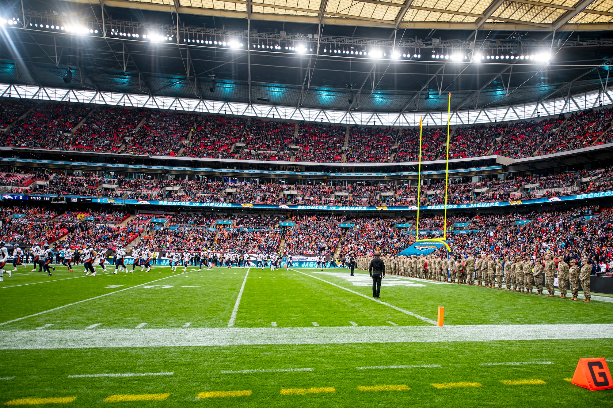 The Denver Broncos, left, run onto the field prior to the national anthem at Wembley Stadium, in London, England, Oct. 30, 2022. Approximately 70 uniformed personnel represented the U.S. Air Force and nation by unveiling an American flag during the pre-game ceremonies of the Jacksonville Jaguars and Denver Broncos NFL game. (U.S. Air Force photo by Staff Sgt. Eugene Oliver)