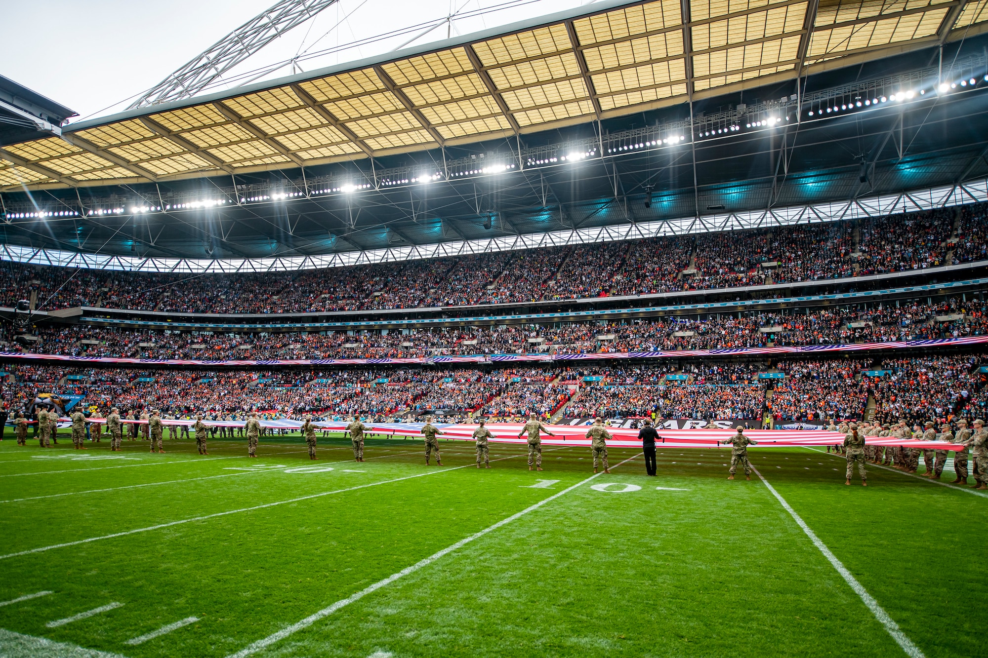 Airmen from the 501st Combat Support Wing unveil an American flag during the national anthem at Wembley Stadium, in London, England, Oct. 30, 2022. Approximately 70 uniformed personnel represented the U.S. Air Force and nation by unveiling an American flag during the pre-game ceremonies of the Jacksonville Jaguars and Denver Broncos NFL game. (U.S. Air Force photo by Staff Sgt. Eugene Oliver)